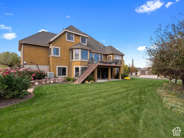 Stucco exterior residence featuring an elevated deck with metal railing, an exterior staircase, a covered lower-level patio, and natural stone landscaping elements