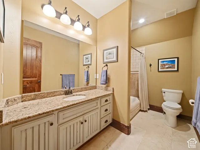 Bathroom featuring a stone-top vanity with off-white beaded cabinetry, large-scale vanity mirror, four-light fixture, tile flooring, and a combined tub and shower enclosure with tile surround