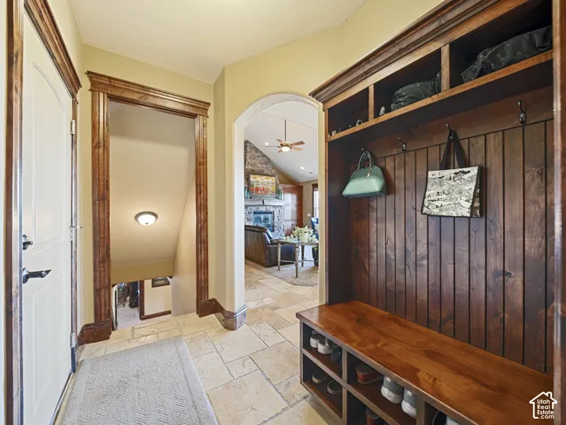 Built-in wood mudroom cabinetry featuring vertical paneling, integrated bench seating, open shelving, and coat hooks, complemented by stone-tile flooring and arched passage framing with heavy wood trim