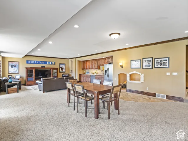 Open-concept area featuring recessed lighting, a wet bar with wooden cabinetry, stainless steel refrigerator, stone flooring inlay, and crown molding