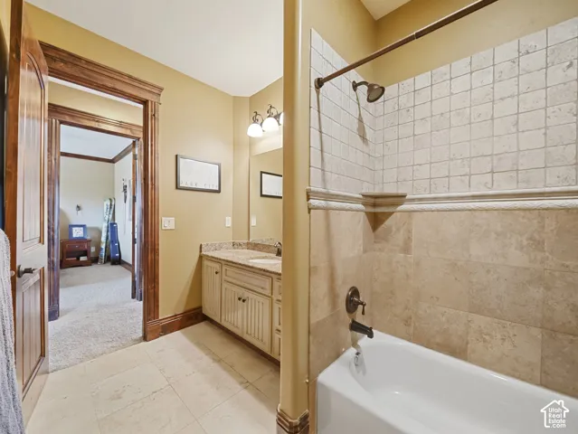Bathroom featuring a tub with a stone-tile surround, dual-tone vanity with a stone countertop, stone flooring, and detailed wood door trim