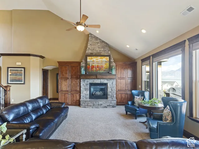 Vaulted ceilings, stone-surround fireplace, custom built-in cabinetry, recessed lighting, and large windows with casing trim