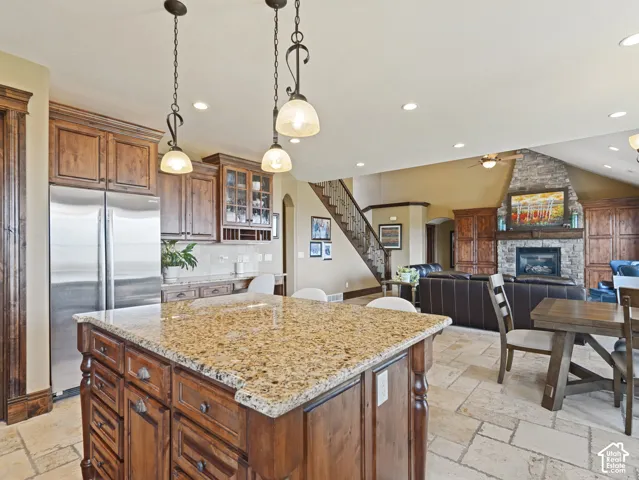 Kitchen featuring a stone-topped island, wooden cabinetry, stone flooring, recessed lighting, and pendant fixtures, complemented by a floor-to-ceiling stone fireplace