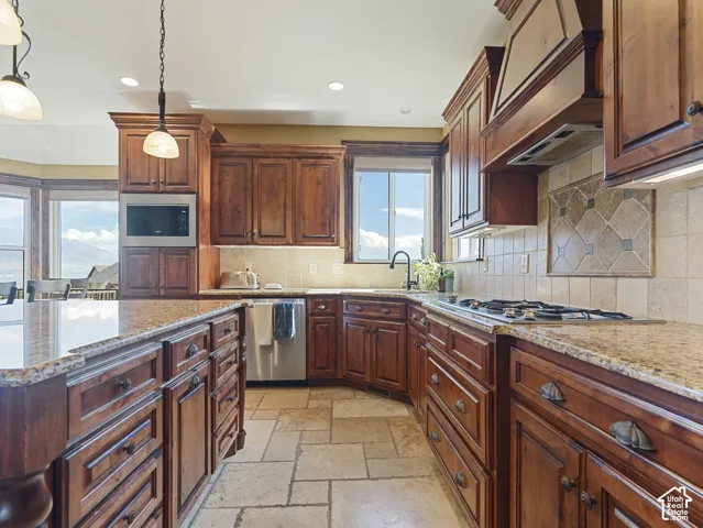 Kitchen featuring natural wood cabinetry, stone countertops, integrated stainless steel appliances, tile flooring, and decorative tile backsplash