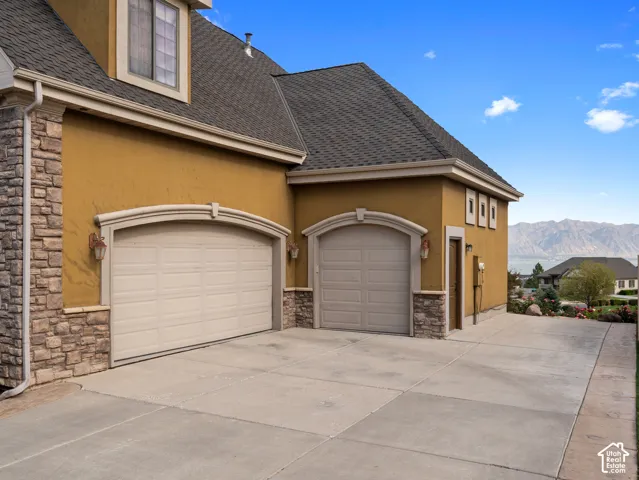 Stucco and stone exterior featuring a three-car garage with arched entryways, concrete driveway, and mountain scenery
