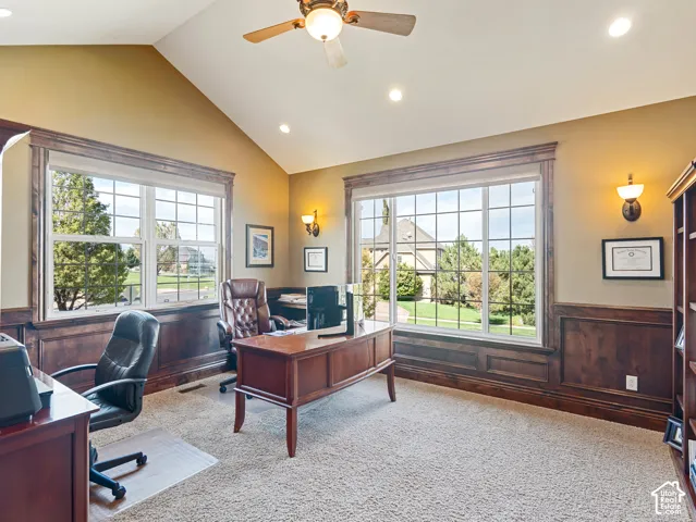 Vaulted ceilings with a ceiling fan, extensive wood-paneled wainscoting, large picture windows, and integrated wall-mounted lighting