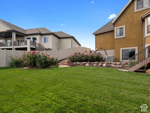 Backyard featuring a manicured lawn, stone retaining walls, rose bushes, and a vinyl privacy fence