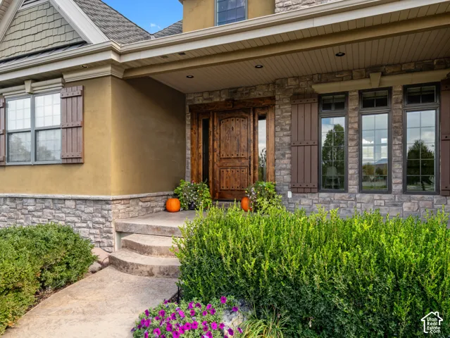 Exterior facade featuring stacked stone masonry, stucco siding, arched wood-finish entry door with side windows, and exterior shutter accents