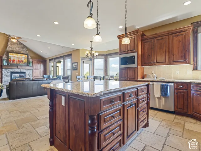 Kitchen featuring custom wood cabinetry, stone-topped center island, natural stone flooring, and pendant lighting