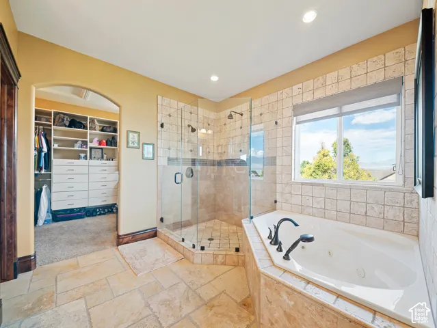 Jetted soaking tub with tile surround, glass-enclosed shower, stone flooring, and built-in walk-in closet cabinetry