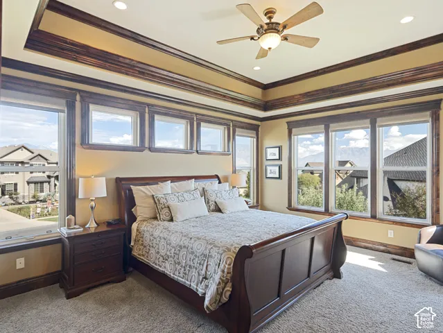 Tray ceiling featuring extensive crown molding, recessed lighting, central ceiling fan, and multiple windows with deep wood-finish trim
