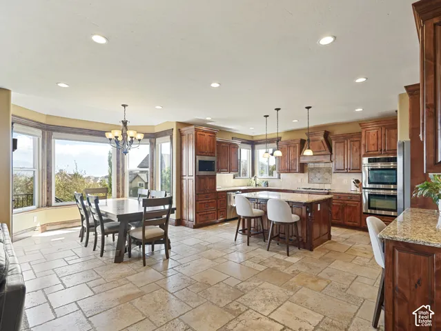 Kitchen featuring natural stone tile flooring, stained wood cabinetry, stone-topped central island, built-in double wall ovens, and recessed lighting