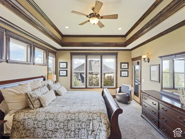 Tray ceiling featuring intricate wood crown molding, multi-pane windows, and a central ceiling fan with integrated light fixture