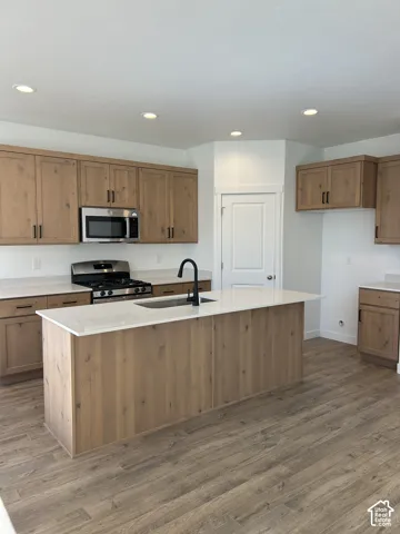 Kitchen featuring wood-finish cabinetry, white countertops, a center island with an undermount sink, a matte black faucet, and recessed ceiling lighting