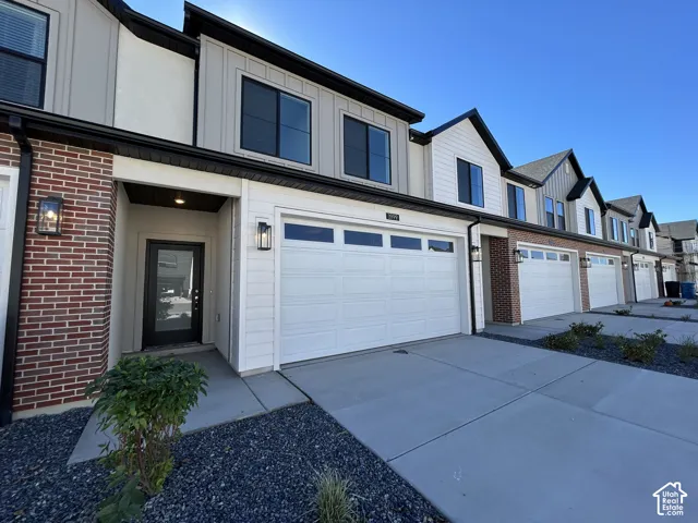 Multi-level townhome exterior featuring red brick masonry, white horizontal lap siding, vertical board-and-batten siding, a two-car garage with a glass-paneled door, and dark metal exterior sconces