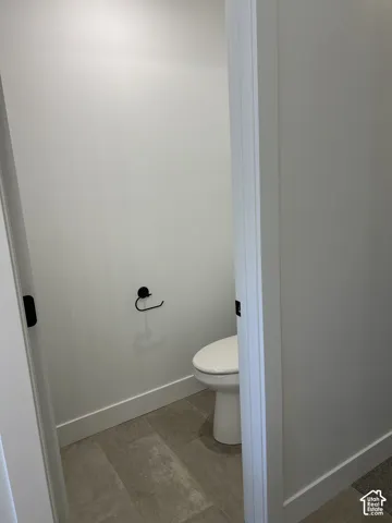 Restroom featuring tile flooring, a white porcelain toilet, and a matte black toilet paper holder