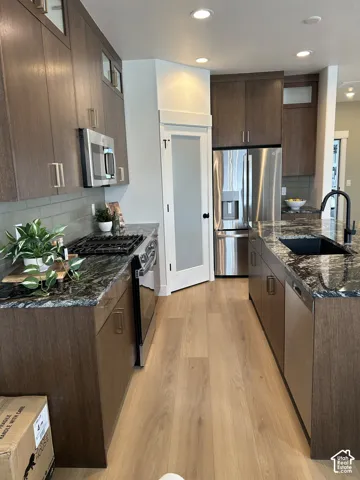 Kitchen featuring dark wood-finish cabinetry, stone countertops, stainless steel appliances, a center island with a recessed sink, and frosted glass pantry door