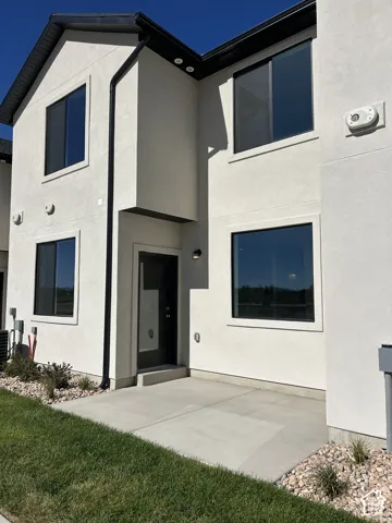 Two-story exterior featuring light-toned stucco siding, a concrete patio, and large glass windows with dark trim