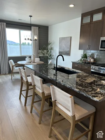 Kitchen featuring a large island with dark stone countertop, matte black undermount sink, and matching faucet, wood-finish flooring, full-height cabinetry with upper glass-front panels, and horizontal plank accent wall