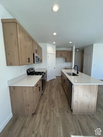 Kitchen featuring flat-panel wood-finish cabinetry, white countertops, a center island with an undermount sink and matte black faucet, and wood-finish flooring