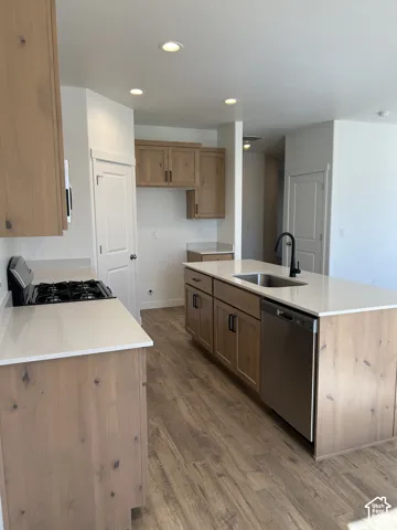 Kitchen featuring wood-finish cabinetry, neutral solid-surface countertops, wood-finish flooring, a stainless steel dishwasher, and a matte black gooseneck faucet