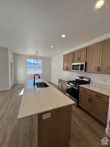 Kitchen featuring wood-finish cabinetry, quartz countertops, central island with undermount sink, stainless steel appliances, and wood-finish flooring