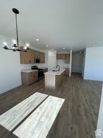 Kitchen featuring wood-finish cabinetry, an island with a light-toned countertop, wood-finish flooring, recessed lighting, and a multi-light chandelier
