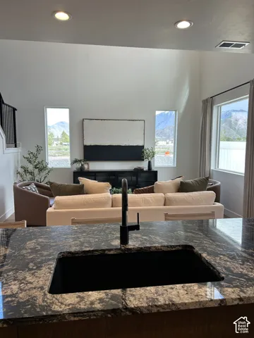Kitchen island with patterned stone countertop, undermount sink, and matte black fixture, featuring high ceilings and mountain scenery through expansive windows