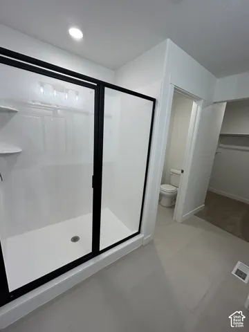 Walk-in shower with matte black framing, integrated shelving, and white surround, paired with neutral large-format tile flooring and recessed lighting