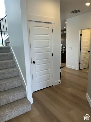Interior featuring wood-finish flooring, five-panel shaker-style interior doors, matte black hardware, and carpeted stairs with a metal balustrade