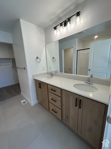Double vanity featuring light-toned cabinetry, quartz countertops, dual integrated sinks, matte black hardware, and a four-bulb industrial-style light fixture