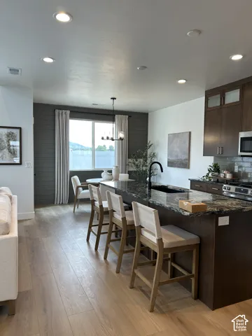 Kitchen featuring dark wood-finish cabinetry, a large stone-topped island with an integrated basin, matte black faucet, and recessed lighting