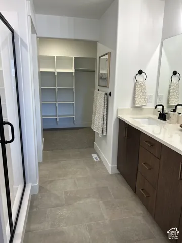 Bathroom featuring a vanity with wood-finish cabinetry, quartz countertop, and matte black hardware, tile flooring, and an integrated walk-in closet with built-in shelving
