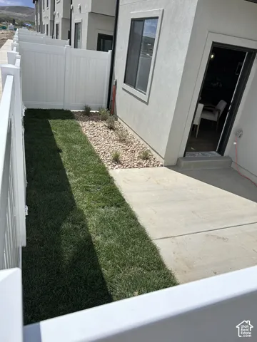 Private exterior space featuring a concrete patio, a section of lawn, decorative stone landscaping, and a white vinyl privacy fence