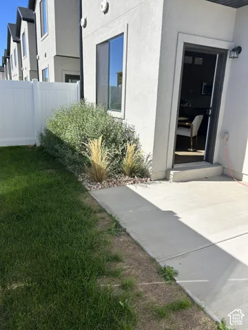 Concrete patio featuring a low-maintenance landscaped bed with stone ground cover, mature shrubbery, and a white vinyl privacy fence