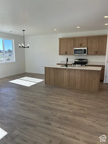 Kitchen featuring wood-finish cabinetry, a center island with a stone-composite countertop, stainless steel appliances, recessed lighting, and wood-finish flooring