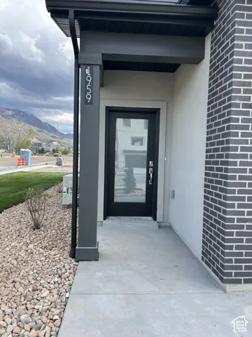 Covered entryway featuring a concrete porch, dark brick siding, smooth stucco finish, and a glass-paneled entry door with mountain backdrop