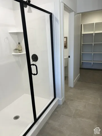 Walk-in shower featuring a glass enclosure with matte black hardware, integrated shelving, large-format neutral tile flooring, and built-in closet shelving