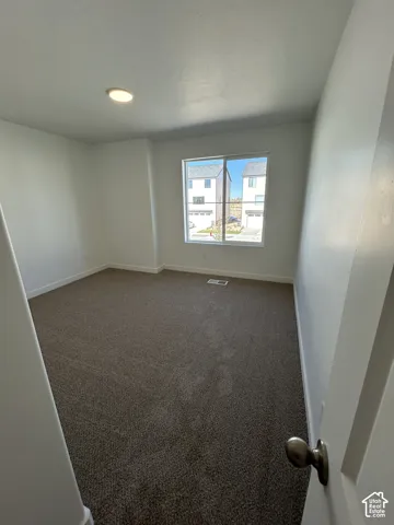 Neutral interior room featuring neutral-tone carpeting, smooth walls, and a large sliding window with grid detail