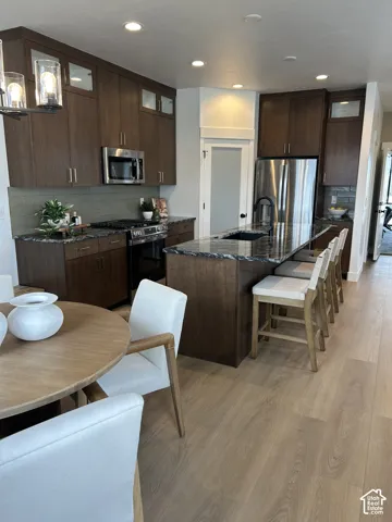 Kitchen featuring dark wood cabinetry, a central island with a contrasting stone countertop and integrated sink, stainless steel appliances, and wood-finish flooring