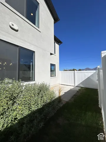 Exterior side yard featuring stucco siding, black-framed windows, a concrete patio, a white vinyl privacy fence, and mountain scenery
