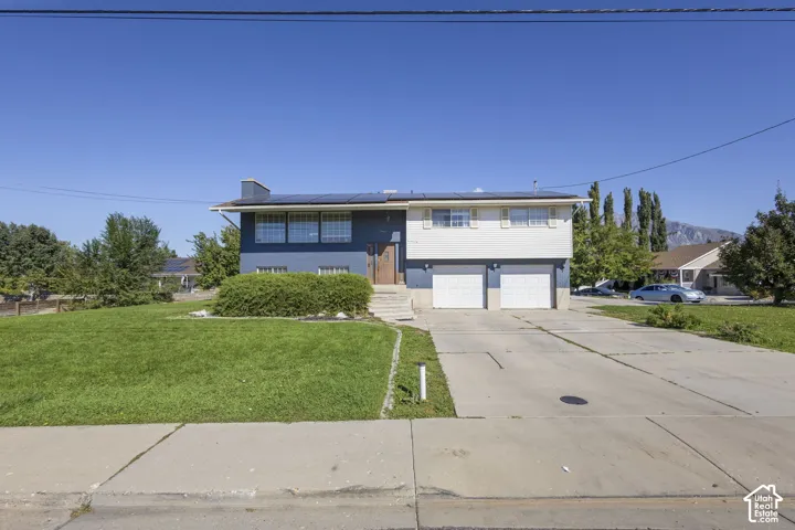 Split-level exterior featuring a two-tone blue and white facade, integrated solar panels, attached two-car garage, and concrete driveway