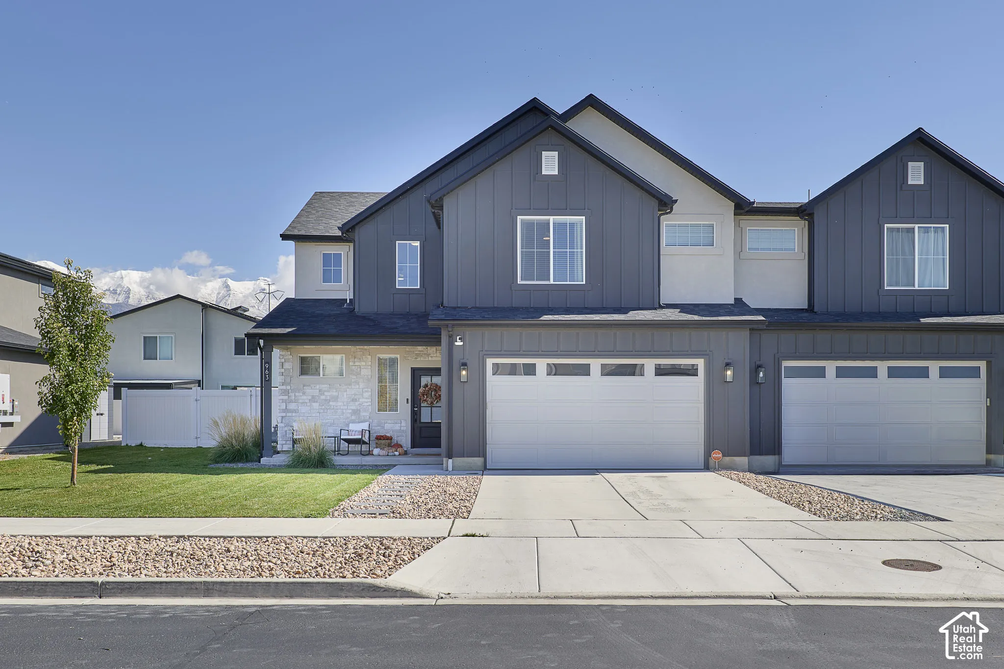 Modern two-story exterior featuring vertical siding, stone veneer accents, multi-gabled roofline, concrete driveway, and a two-car garage