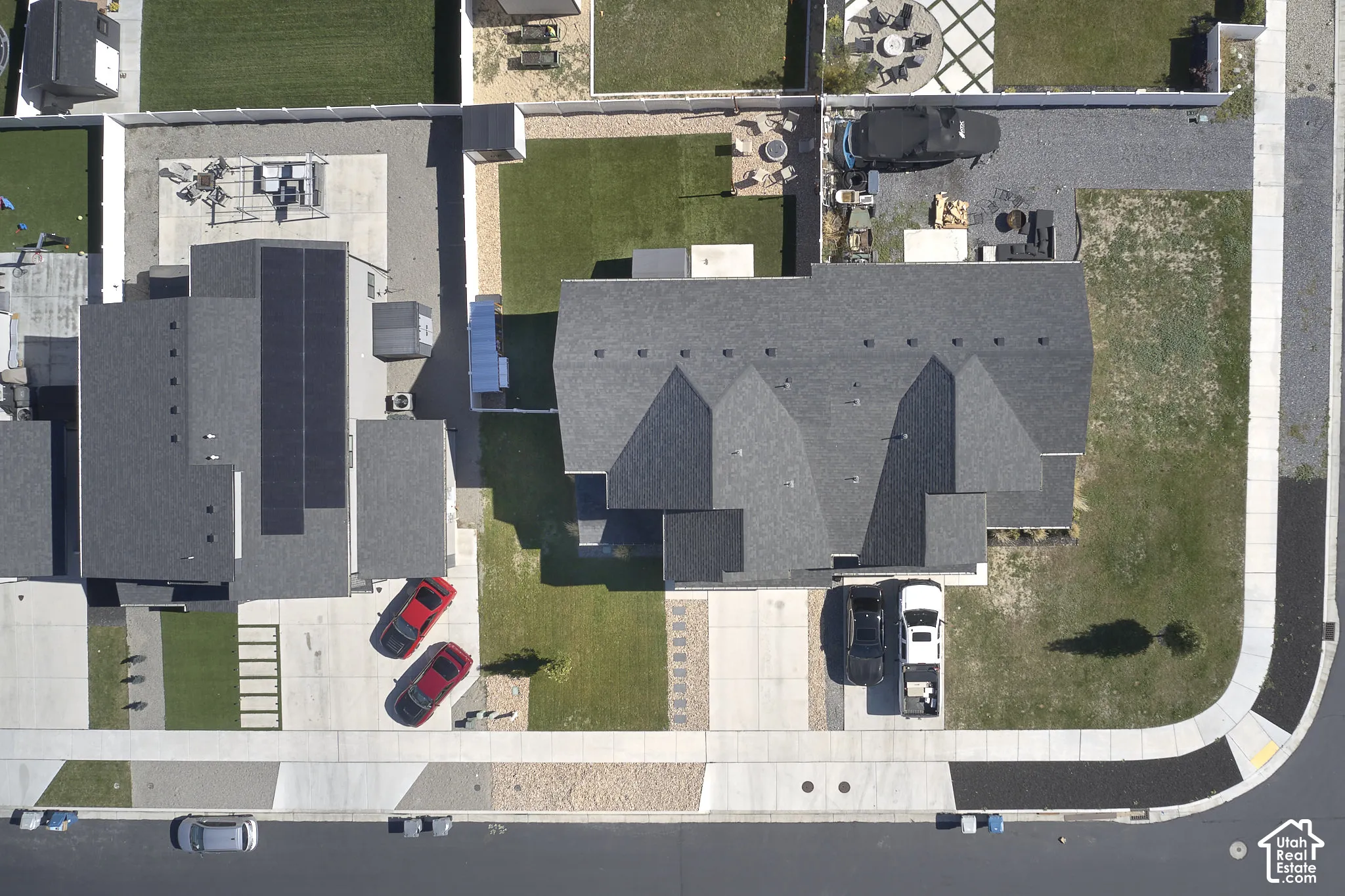 Aerial perspective of the property featuring a gabled roofline with integrated solar panels, concrete driveway, and enclosed backyard with manicured lawn