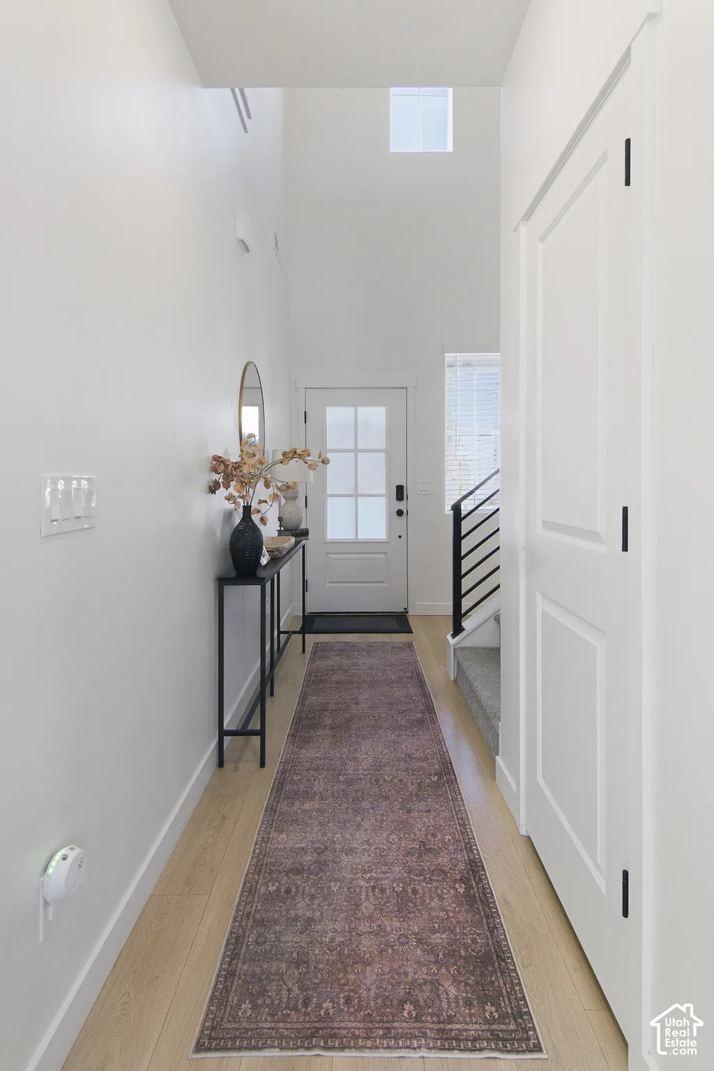 Foyer featuring high ceilings, light-tone wood-finish flooring, a multi-pane glass-panel entry door, and a staircase with a modern metal railing