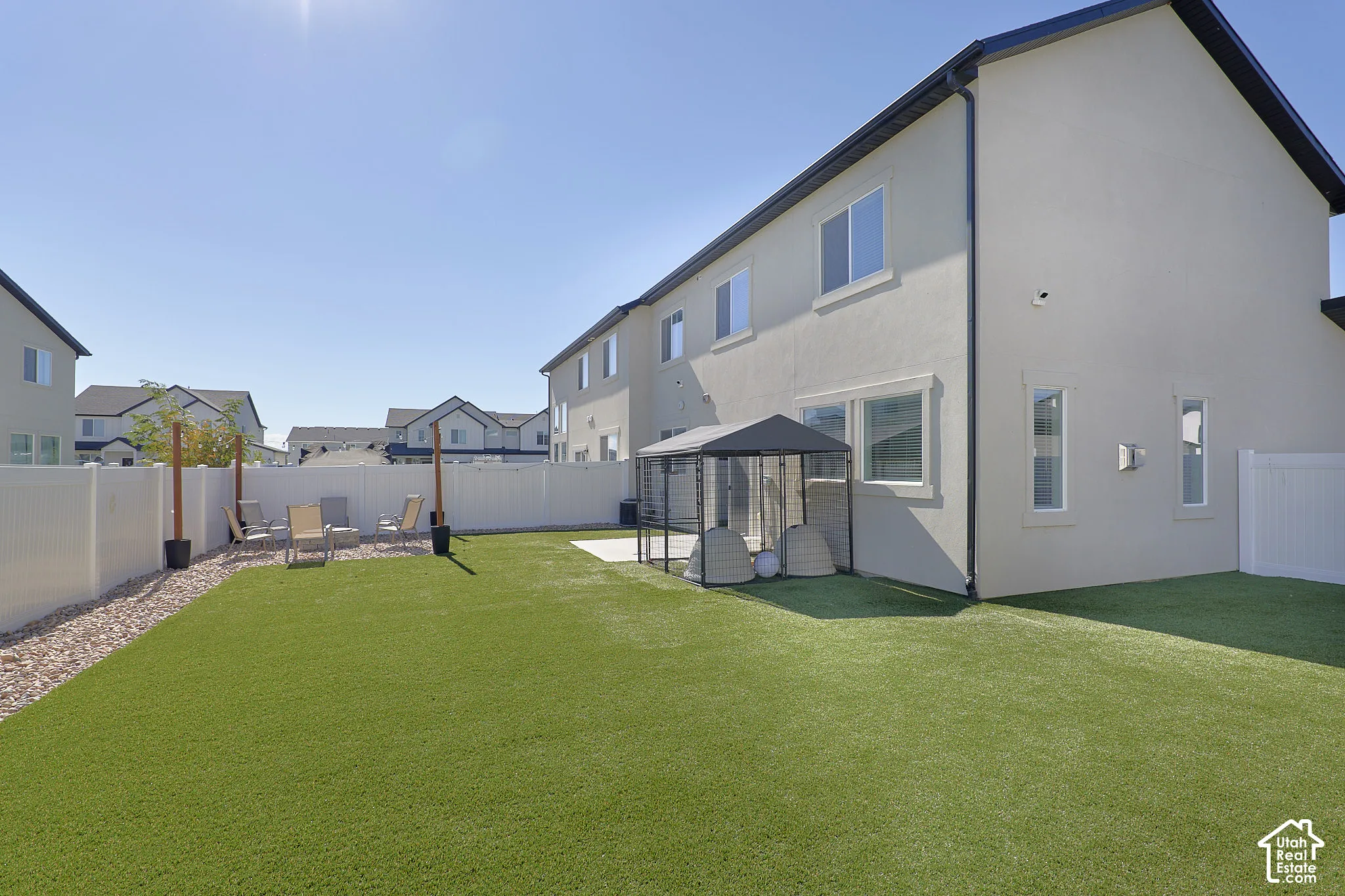 Backyard featuring synthetic turf, concrete patio, white vinyl perimeter fencing, and a graveled area
