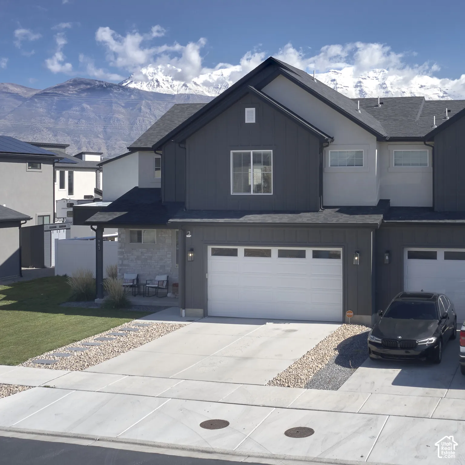 Two-story exterior featuring vertical dark siding, stone veneer accents, an attached two-car garage, and snow-capped mountain backdrop