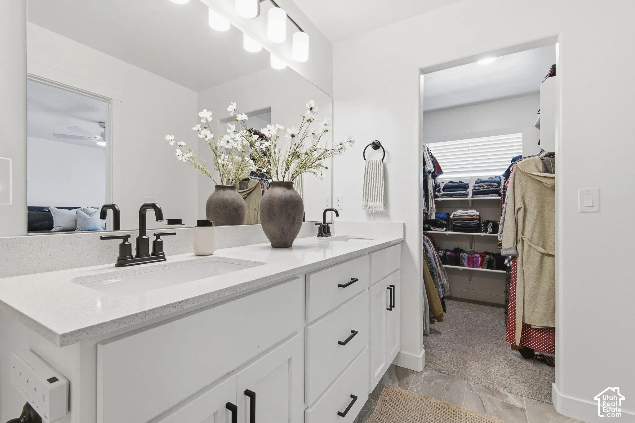 Dual-sink vanity with a quartz countertop, matte black fixtures, white cabinetry, and a full-width mirror
