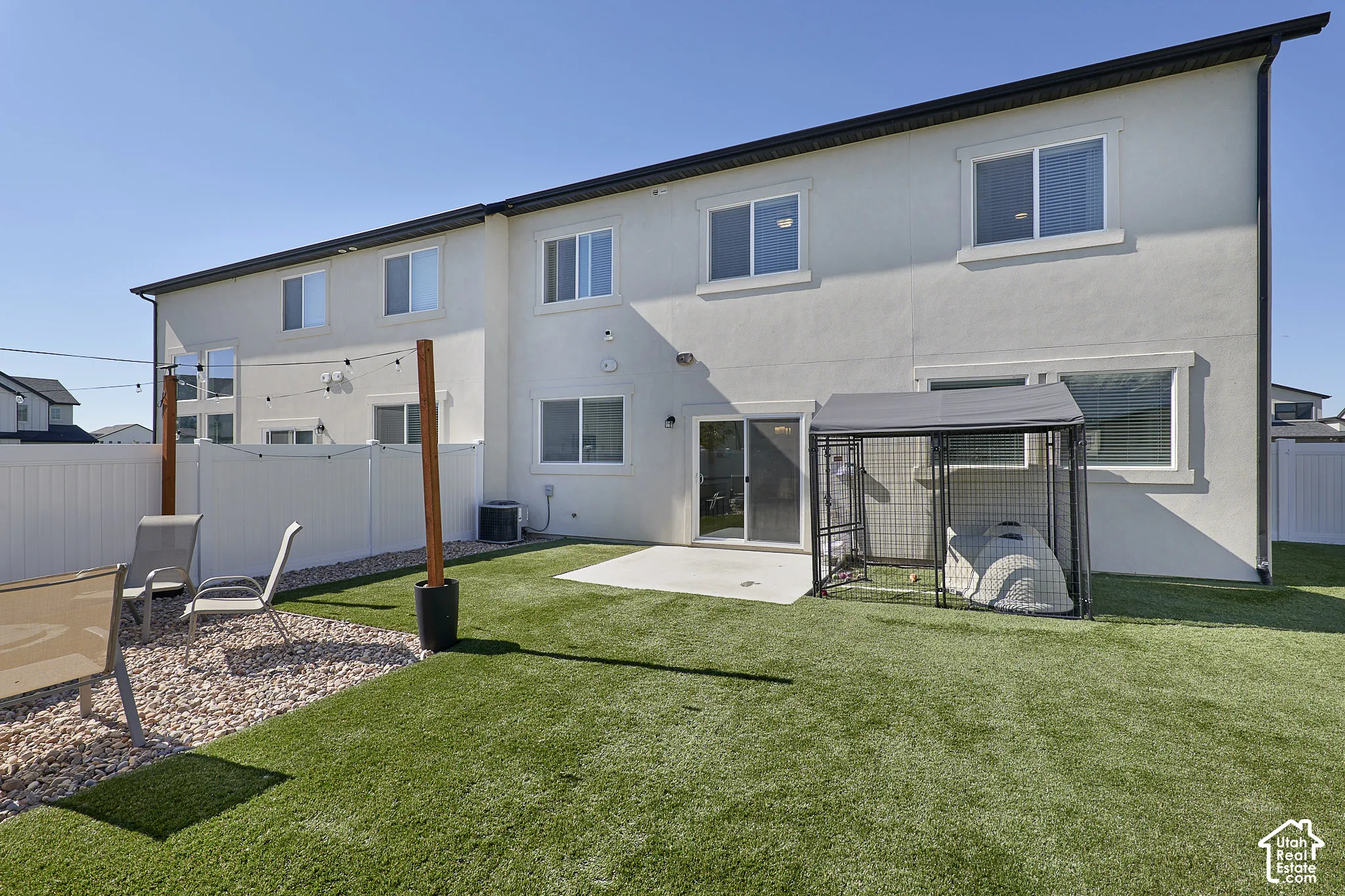 Fenced backyard featuring synthetic turf, concrete patio, and stone ground cover