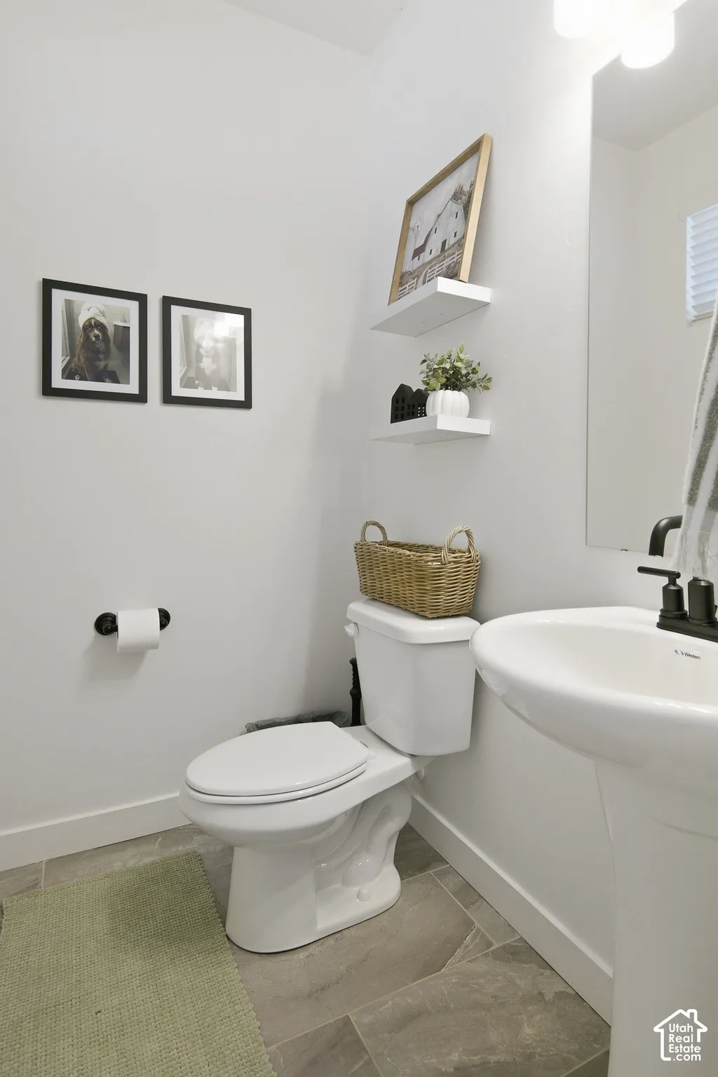 Powder room featuring a pedestal sink, matte black faucet, large-format tile flooring, wall-mounted shelving, and a vanity mirror with overhead lighting